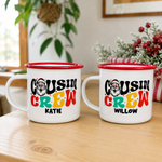 Two red-rimmed Santa Cousin Crew enamel mugs personalised with the names Katie and Willow