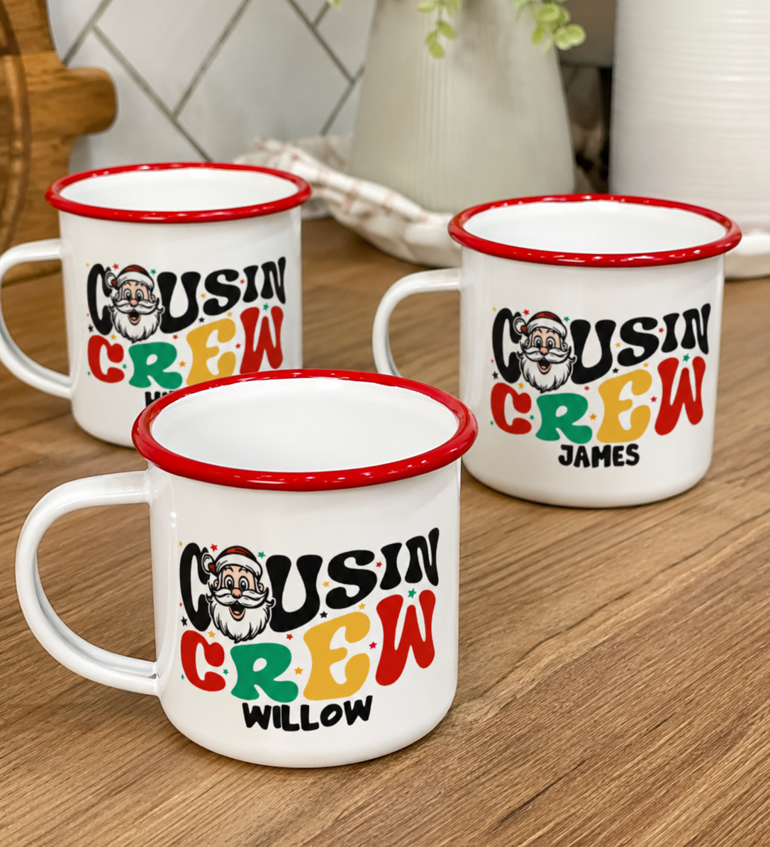 Three personalised Santa Cousin Crew enamel mugs on a wooden bench, retro Santa print detail - The Custom Co