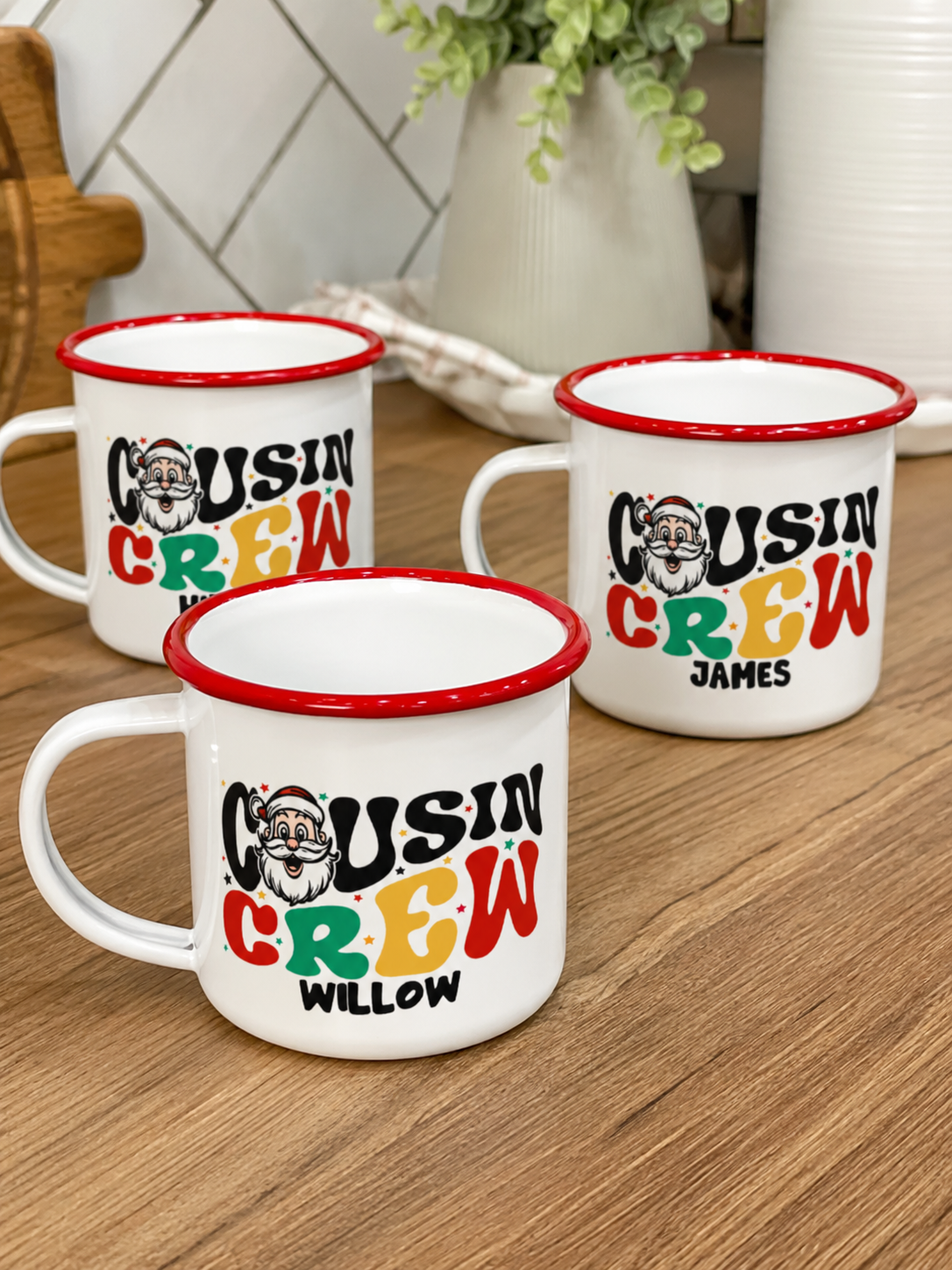 Three personalised Santa Cousin Crew enamel mugs on a wooden bench, retro Santa print detail - The Custom Co
